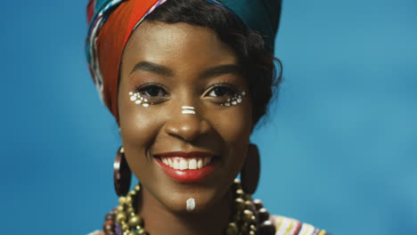 vista de cerca de una joven afroamericana alegre con turbante y maquillaje sonriendo alegremente a la cámara