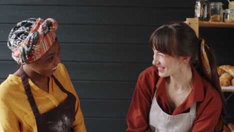 cheerful multiethnic women kneading dough and chatting in bakery