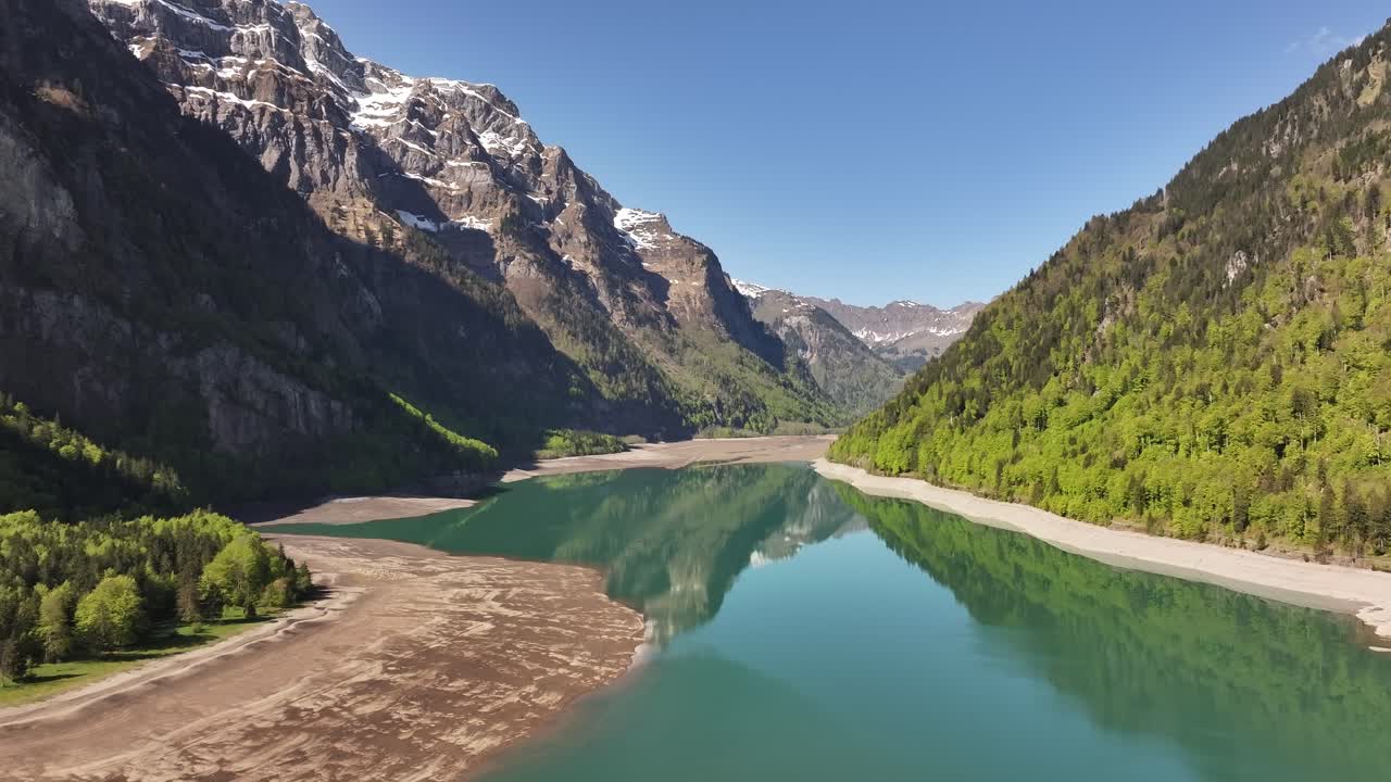 Aerial view of Klöntalersee lake surrounded by green forests and snowy mountains in Glarus, Switzerland