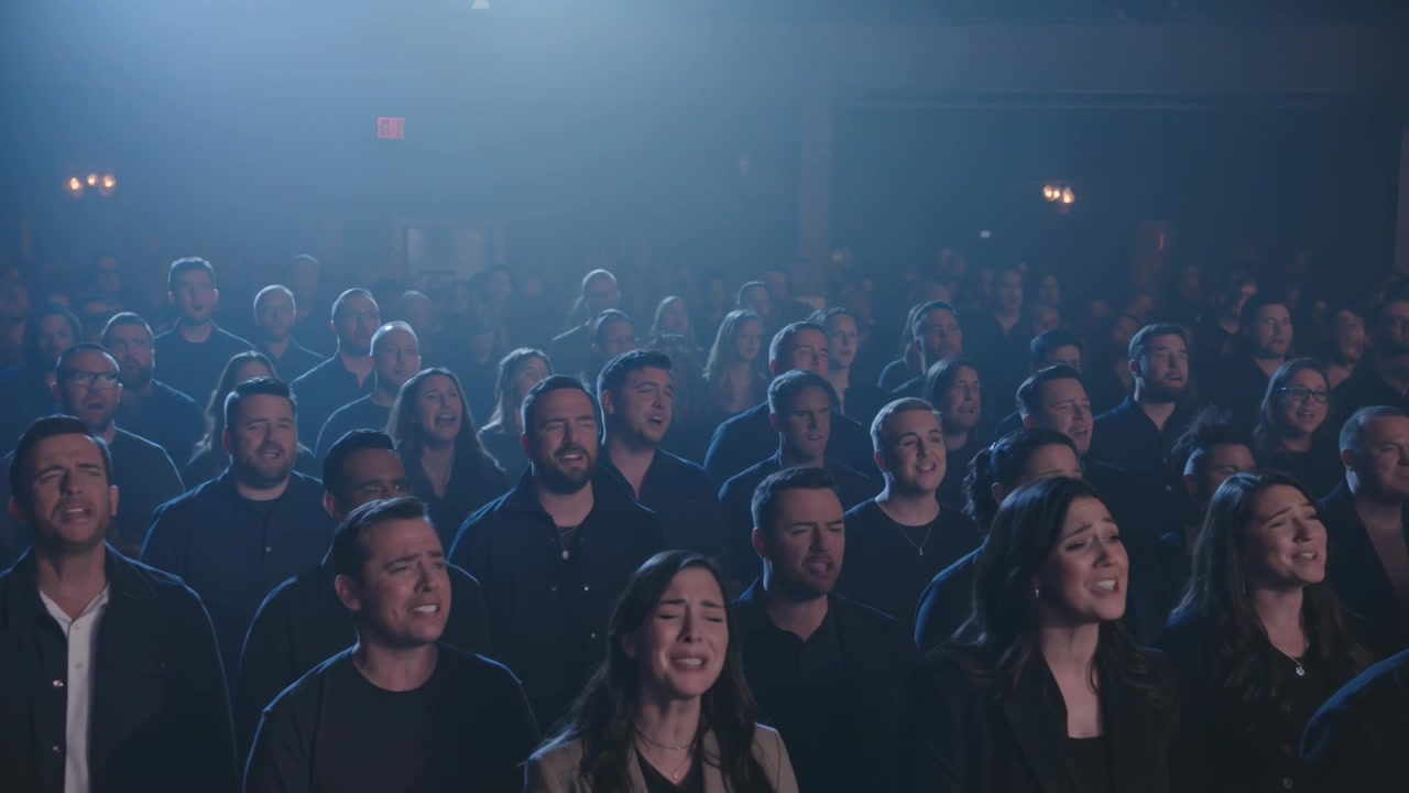 Singendes Publikum folgt musikalischem Einsatz, erhebt Stimmen im Theater mit Scheinwerfern und dunklen Jacken.