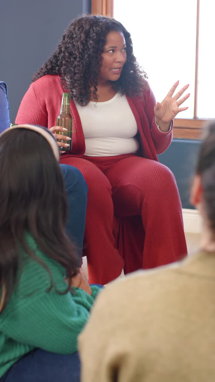Video verticale di una donna afroamericana felice seduta con una birra e che parla con gli amici