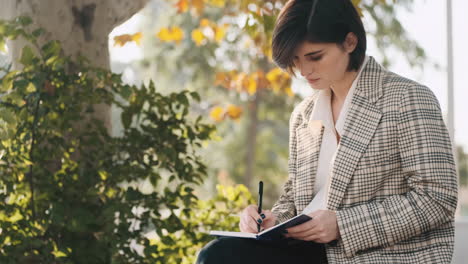 female entrepreneur drawing up business plan for a month in notepad while resting outdoor.