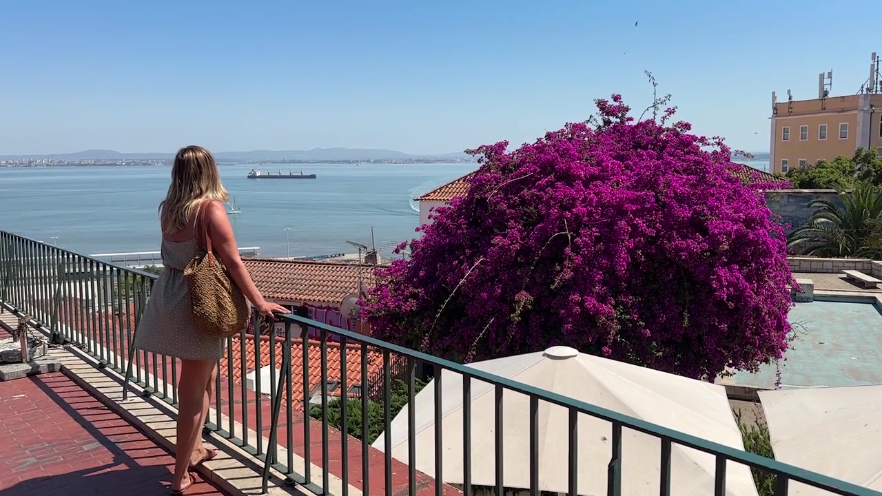 Splendide riprese di una donna che ammira le ampie vedute sull'oceano da uno dei punti panoramici più suggestivi di Lisbona, catturando la bellezza mozzafiato della costa di una delle capitali più amate d'Europa.