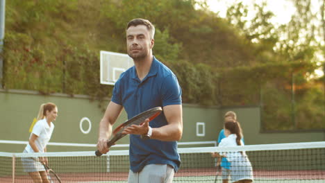 handsome man training with racket while his family playing tennis in the background