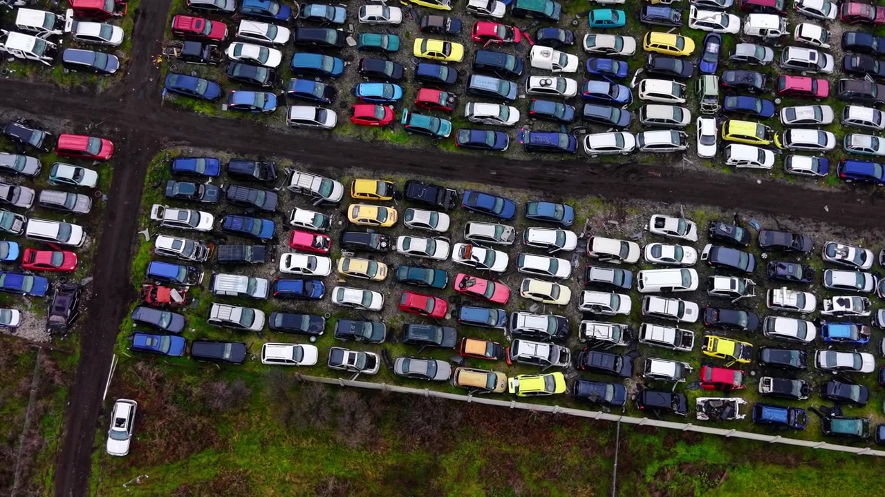 Rækker af farverige ødelagte biler. Luftfoto ovenfra af køretøjer sorteret efter farve langs en smal, opdelende grusvej.