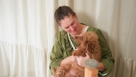 dog owner lifts fluffy brown dog, places it lovingly on her lap, embraces it warmly, and kisses it with affection in cozy indoor setting, expressing deep emotional bond and companionship