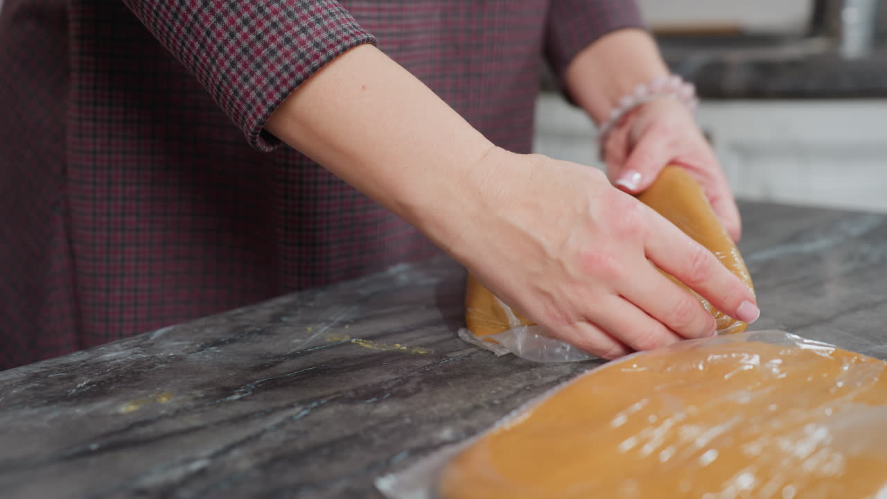 가죽으로 감싸진 반죽을 다른 반죽 위에 놓고, 손목으로 장식된 손으로, 현대 주방의 깨한 카운터에 베이킹 준비를 조심스럽게 준비하는 여성의 클로즈업