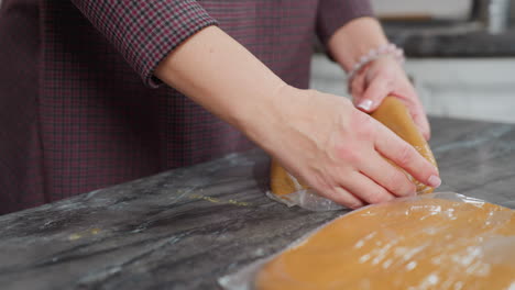 close up de una mujer colocando una masa envuelta en cuero blanco en otra masa con una mano adornada con un brazalete, arreglando cuidadosamente la preparación de horneado en un mostrador limpio en una cocina moderna