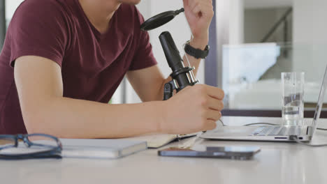 Mid-section-of-asian-boy-speaking-on-professional-microphone-to-record-audio-podcast