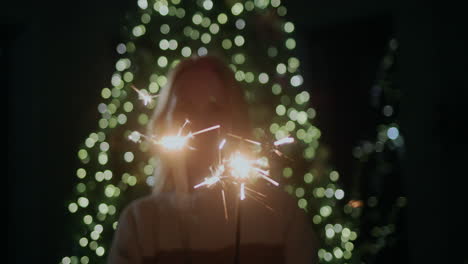 Happy-woman-holding-sparklers,-standing-against-the-backdrop-of-a-Christmas-tree-at-home