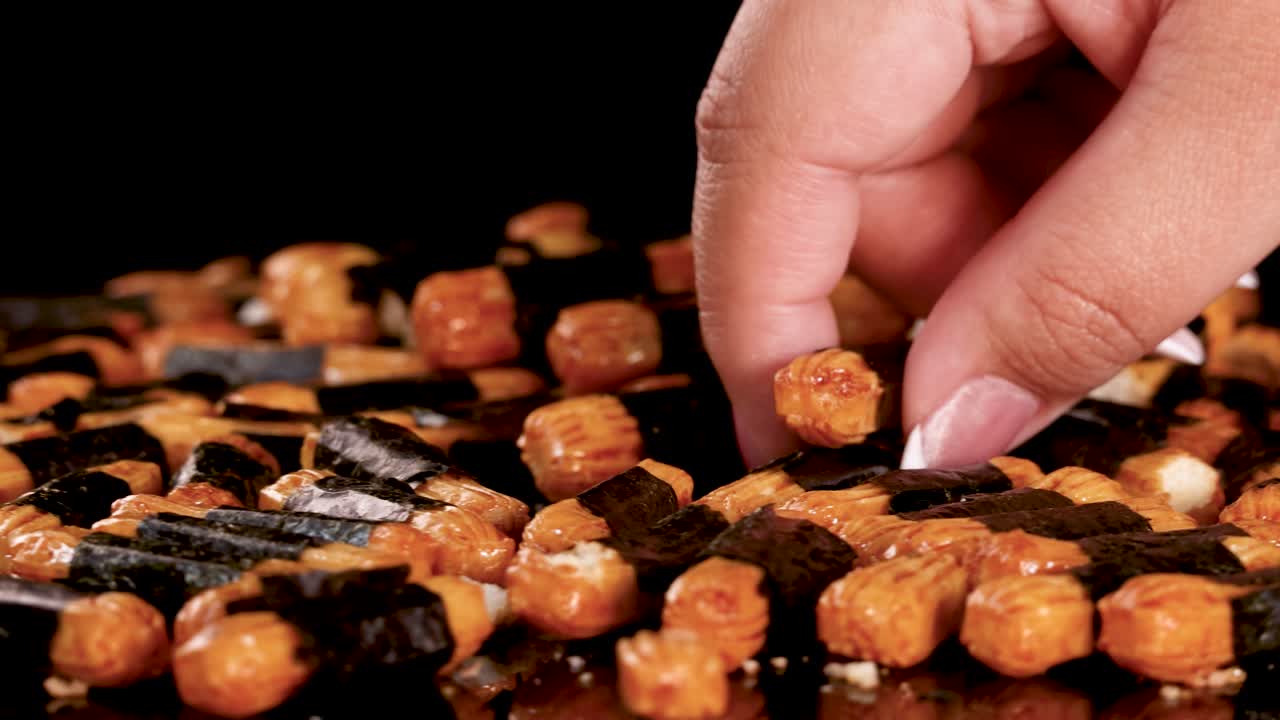Close-up of hand selecting crunchy Japanese rice crackers, dramatic lighting, slow rotating camera movement