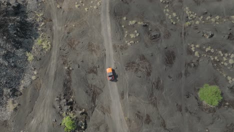 Jeep-Naranja-Conduciendo-Por-Un-Camino-De-Arena-De-Basalto,-Camión-4x4-Fuera-De-La-Carretera-En-Un-Antiguo-Campo-De-Lava,-De-Arriba-Hacia-Abajo