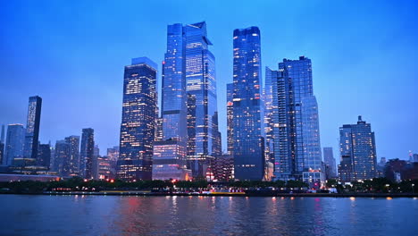 skyscrapers and high-rises switched on lights at dusk time. low angle view on the stunning modern architecture of new york, usa from the river waterscape