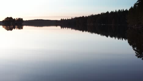 Drohnenschuss,-Der-Bei-Sonnenuntergang-über-Einem-Ruhigen-See-In-Schweden-Fliegt