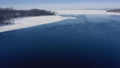 Drone-Volando-Sobre-Un-Río-Cerca-De-Un-Bosque-En-Invierno