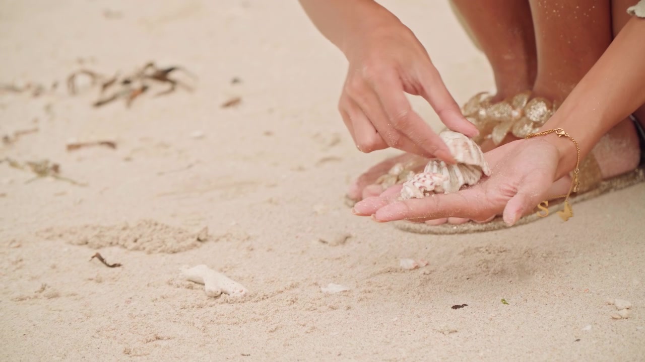 Bare feet and hands on beach sand arranging seashells into palm, woman collects delicate shells while wearing shell bracelet, warm sunlight, soft grainy texture, calm summer mood, seaside treasure