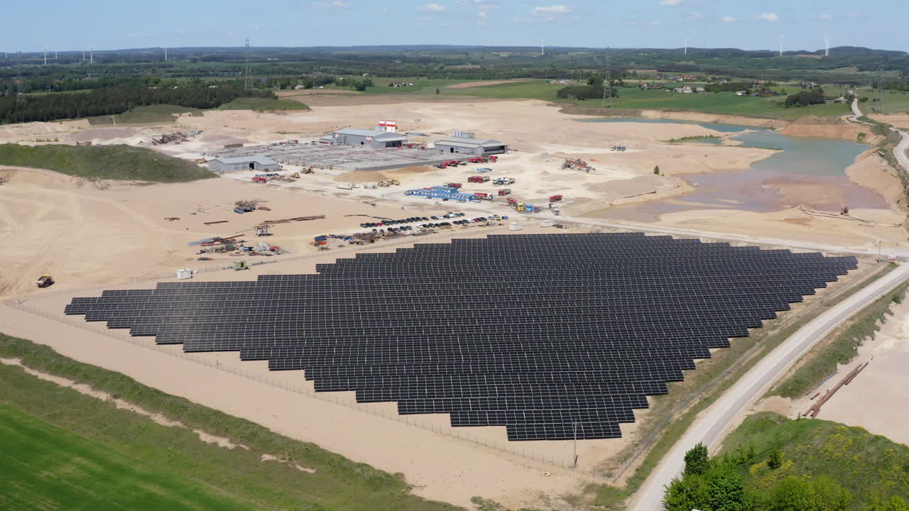 Aerial View Of Solar Farm And Sand Mining Industry With Wind Turbines In Distant Background.