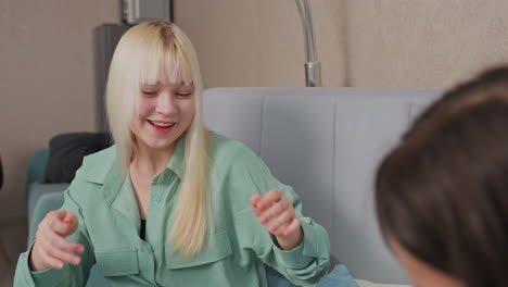 girls engage in playful popcorn fight while sitting on bed in cozy room, blonde girl in green shirt raises hand to dodge incoming popcorn as friend teases her