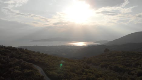 aerial  day drone shot of amazing mountain landscape  green trees small traditional village sun shines behind white clouds sun reflects in the sea at background amazing view