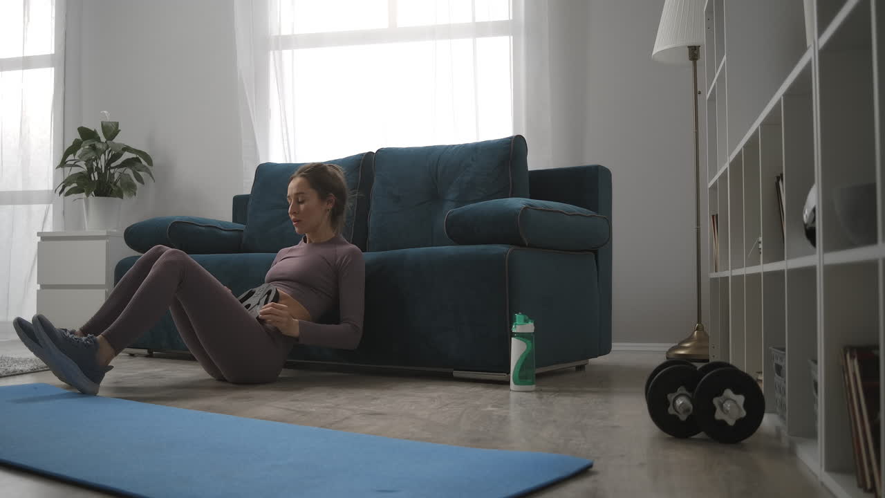 Husmor trener hjemme i stuen om morgenen, strammer mage- og hoftemuskler. Sporty og sunn livsstil for unge moderne kvinner.