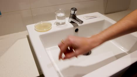 las manos realizan pruebas de bacterias utilizando una placa de petri y un hisopo en un ambiente de fregadero de baño con iluminación brillante