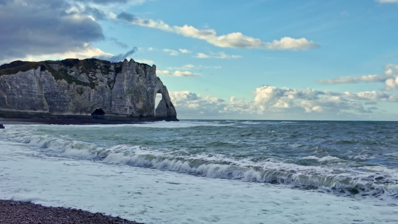 Falaises d'Aval avec arche naturelle de craie et vagues frappant la plage de galets à Étretat, Normandie, France, géologie côtière spectaculaire façonnée par l'érosion le long de la Manche, panoramique horizontal, plan large.