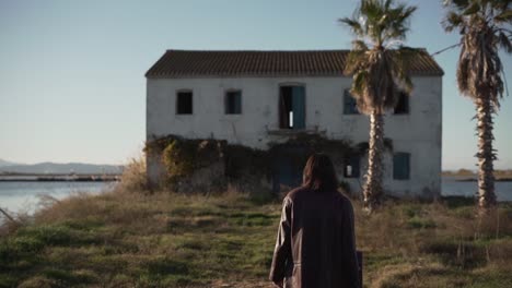 a person walks towards an abandoned house by a marsh