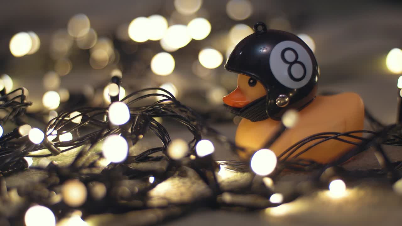 Close-up shot of rubber duck in hand made motorcycle helmet on background of christmas garland