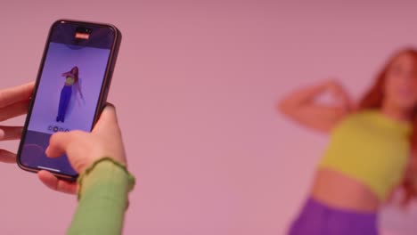 fotografía de estudio de una mujer tomando una foto de una amiga bailando en un teléfono móvil contra un fondo rosa 6