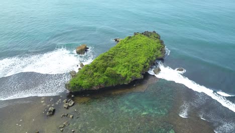 aerial view of big coral rock on the shoreline with clear sea water and waves