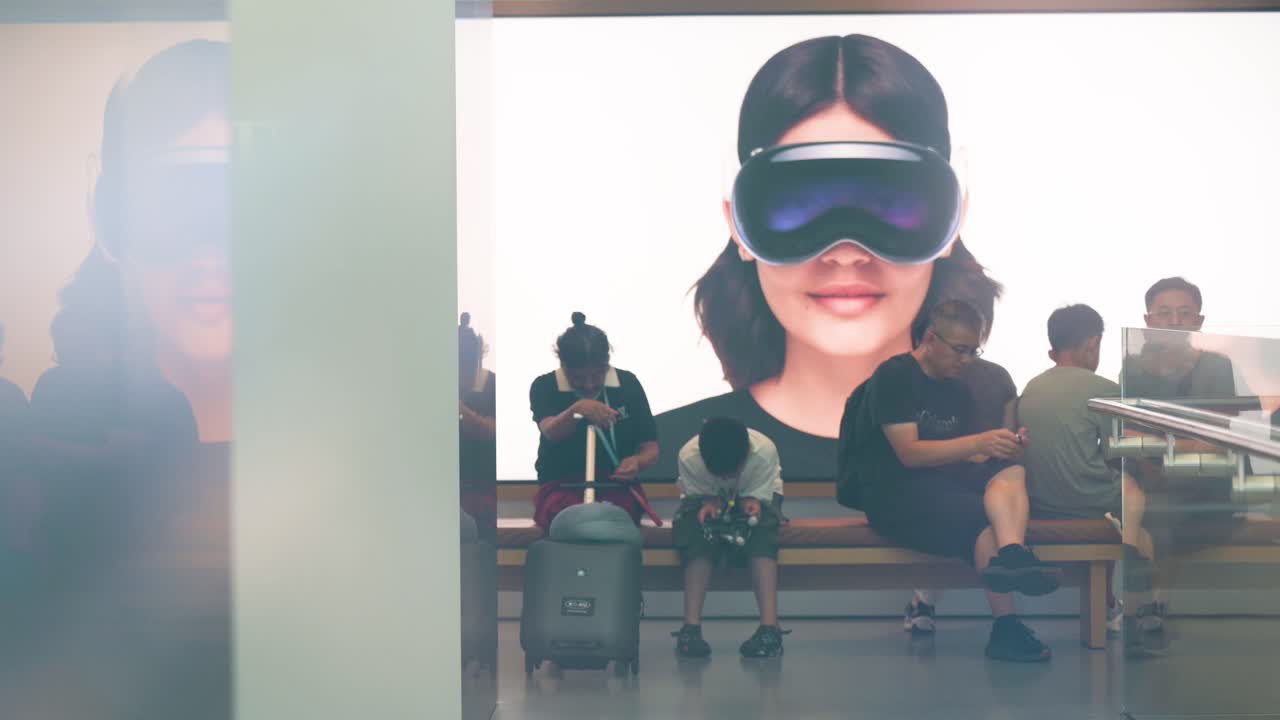 While customers shop at the American tech company's store in Hong Kong, a poster featuring the Apple Vision Pro, Apple's new mixed-reality headset, can be seen in the background.