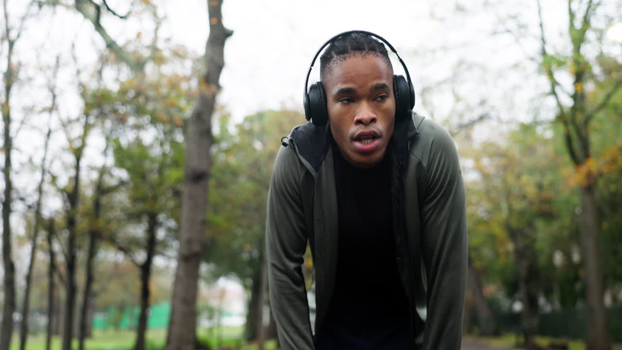 Træt, løber og musik med sort mand i parken