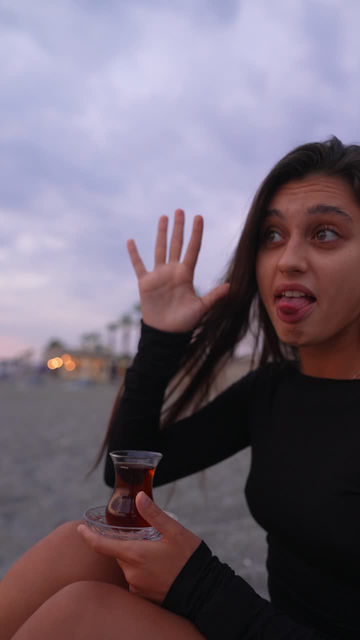 mujer disfrutando de té turco en la playa al atardecer