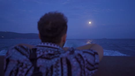 the man looking at the sea and the moon at night.