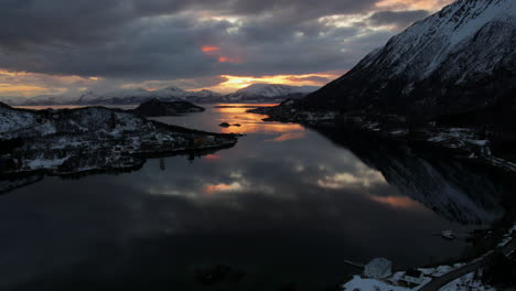 amazing aerial timelapse of beautiful snow covered mountains with moving clouds at sunset mirrored in the glassy calm waters, dolly forward shot