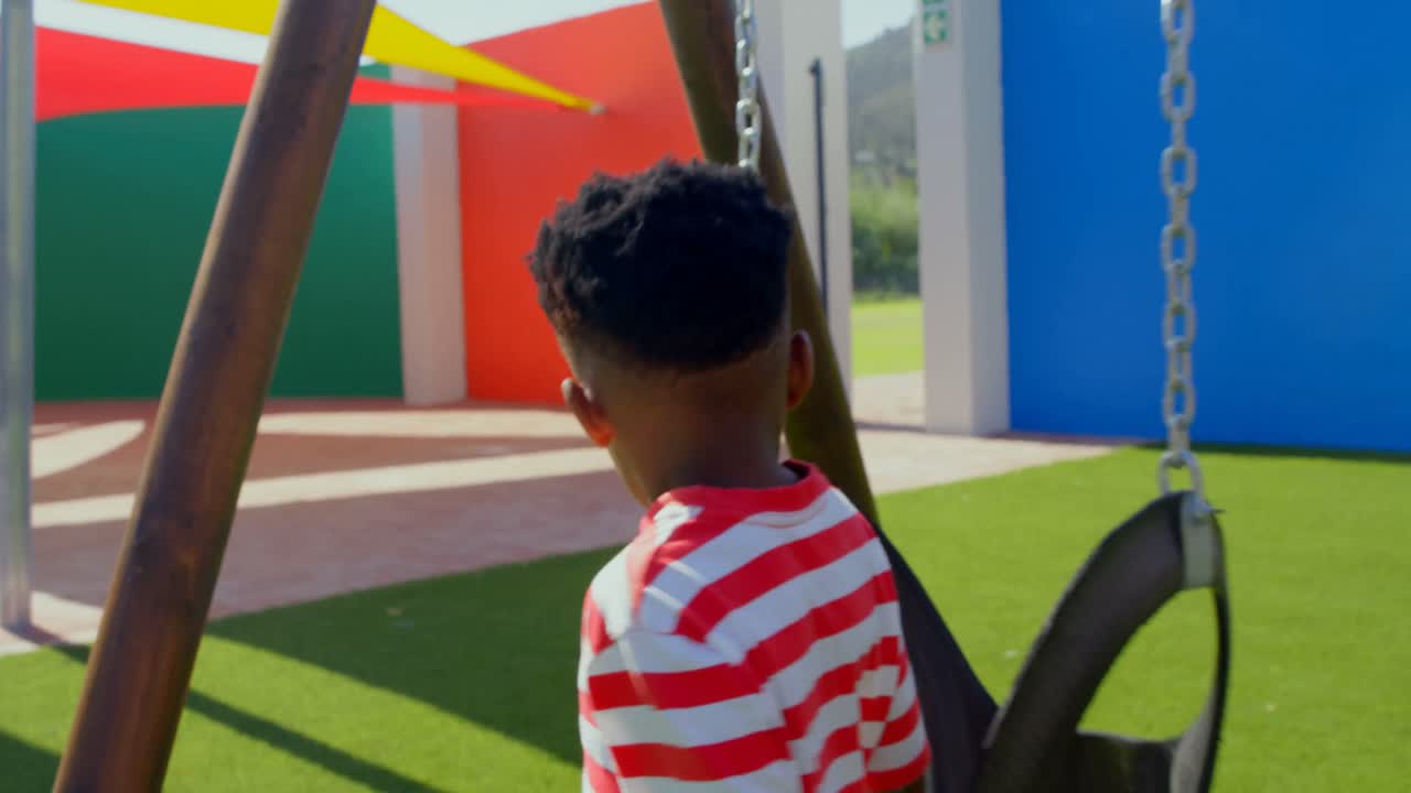 Rear view of African American schoolboy running towards swing in school playground 4k