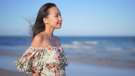 Perfil-De-Una-Joven-Asiática-Vestida-De-Verano-Parada-En-Una-Playa-De-Arena-Con-Una-Ligera-Brisa-En-El-Cabello,-Cámara-Lenta