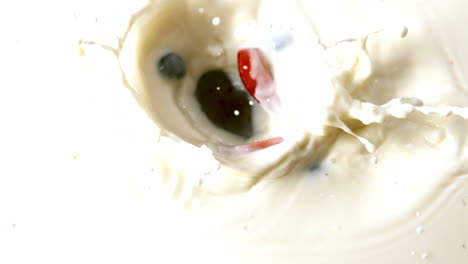 different berries falling in glass of milk