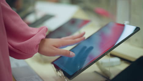 hand in pink dress interacting with a tablet on a display stand in a bright environment, using the screen to operate the device, the tablet is positioned on a sleek stand in a well-lit