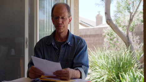 an older middle aged man reading a medical letter giving him bad news that he has been diagnosed with cancer and looking calm and sad but remaining hopeful, positive and optimistic