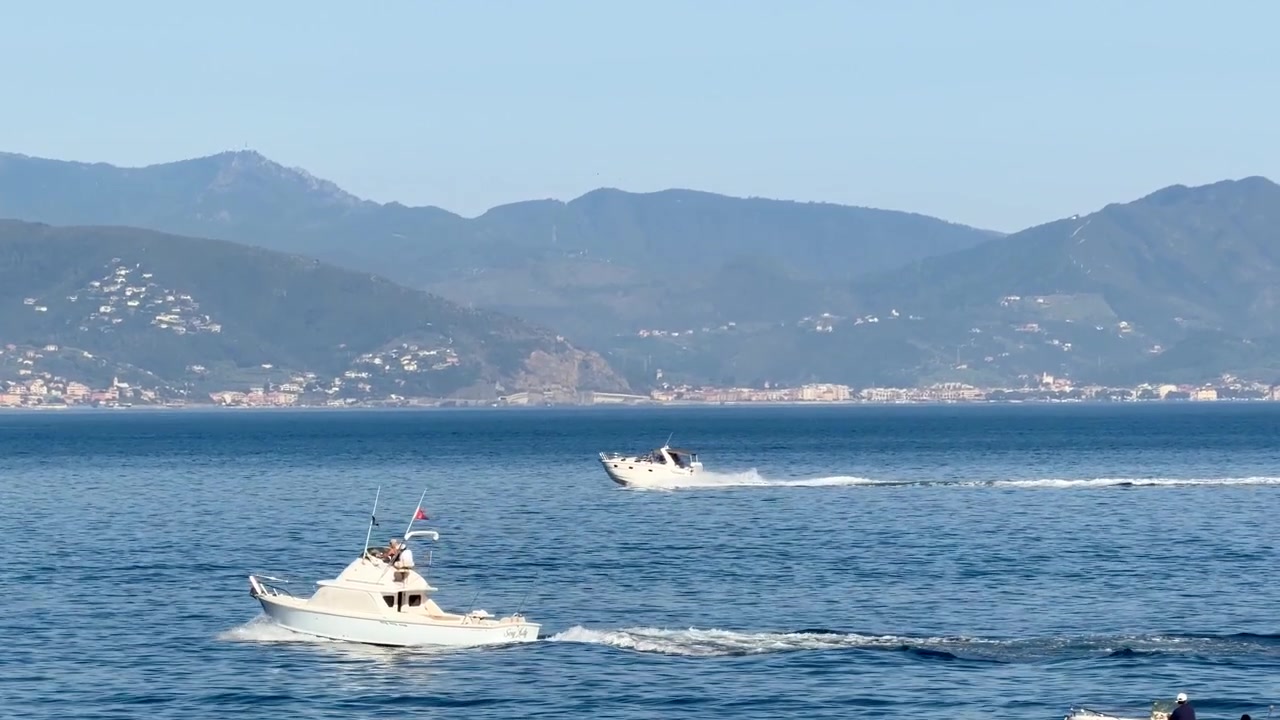 Inquadratura ampia di un motoscafo bianco che naviga su acqua blu calma con montagne sullo sfondo