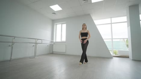 fit girl in black clothes performing contemporary. female dancer shows flowing motions, body and hands waves at white room. modern ballet dance choreography. young woman is moving smoothly