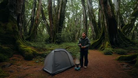 man camping and cooking in a dense, mossy forest