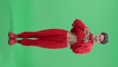 full body of happy young asian transgender male use mobile phone while standing on green screen in the studio
