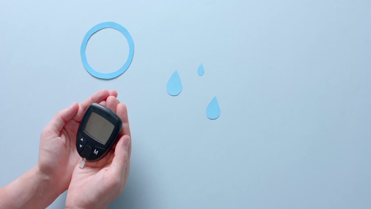Hands of caucasian woman holding glucometer over blue drops and circle on pale blue, slow motion