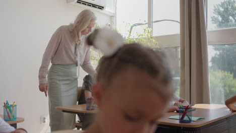 Die-Kinder-Der-Klasse-Sitzen-An-Ihren-Schreibtischen-Und-Der-Lehrer-Geht-Durch-Die-Klasse-Und-Erklärt-Das-Thema-Der-Unterrichtsstunde.-Intelligente-Kinder-Lernen-In-Einer-Freundlichen,-Modernen-Umgebung