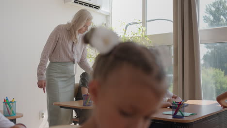 los niños de la clase están sentados en sus escritorios y el maestro camina por la clase y explica el tema de la lección. niños inteligentes aprendiendo en un entorno moderno amigable
