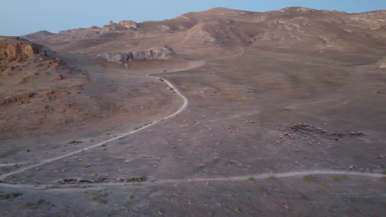 Aerial shot of a desert road surrounded by sparse vegetation and canyon ridges in Utah, filmed at dusk to emphasize soft sky gradients and rugged terrain