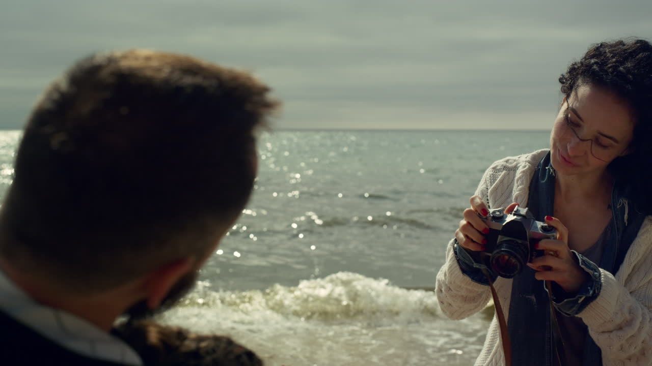 바다의 파도 해변에서 가족 사진을 찍는 여자. 카메라를 사용하는 곱슬머리 소녀.