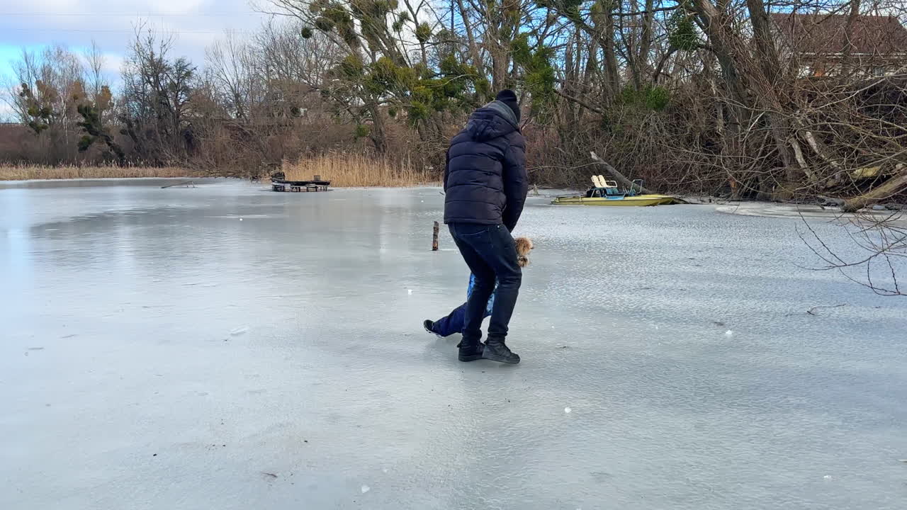 Fun time-spending outdoors in winter. Father turning around on the ice holding his baby son by the hands.
